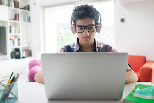 Young man wearing headphones looking at a laptop.